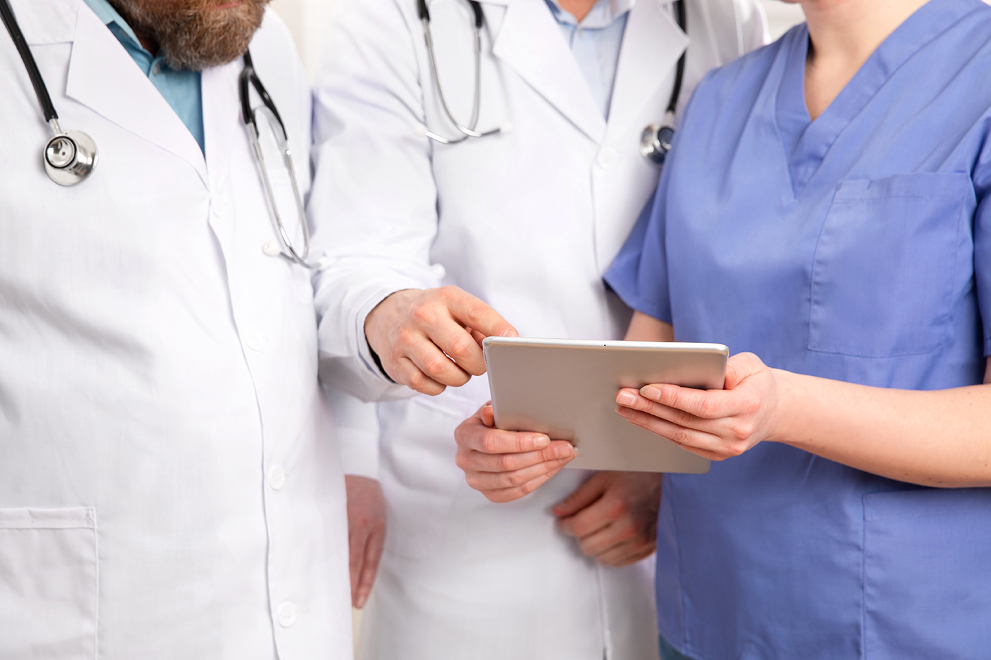 Doctor in medical team discussing patient report at tablet computer in hospital